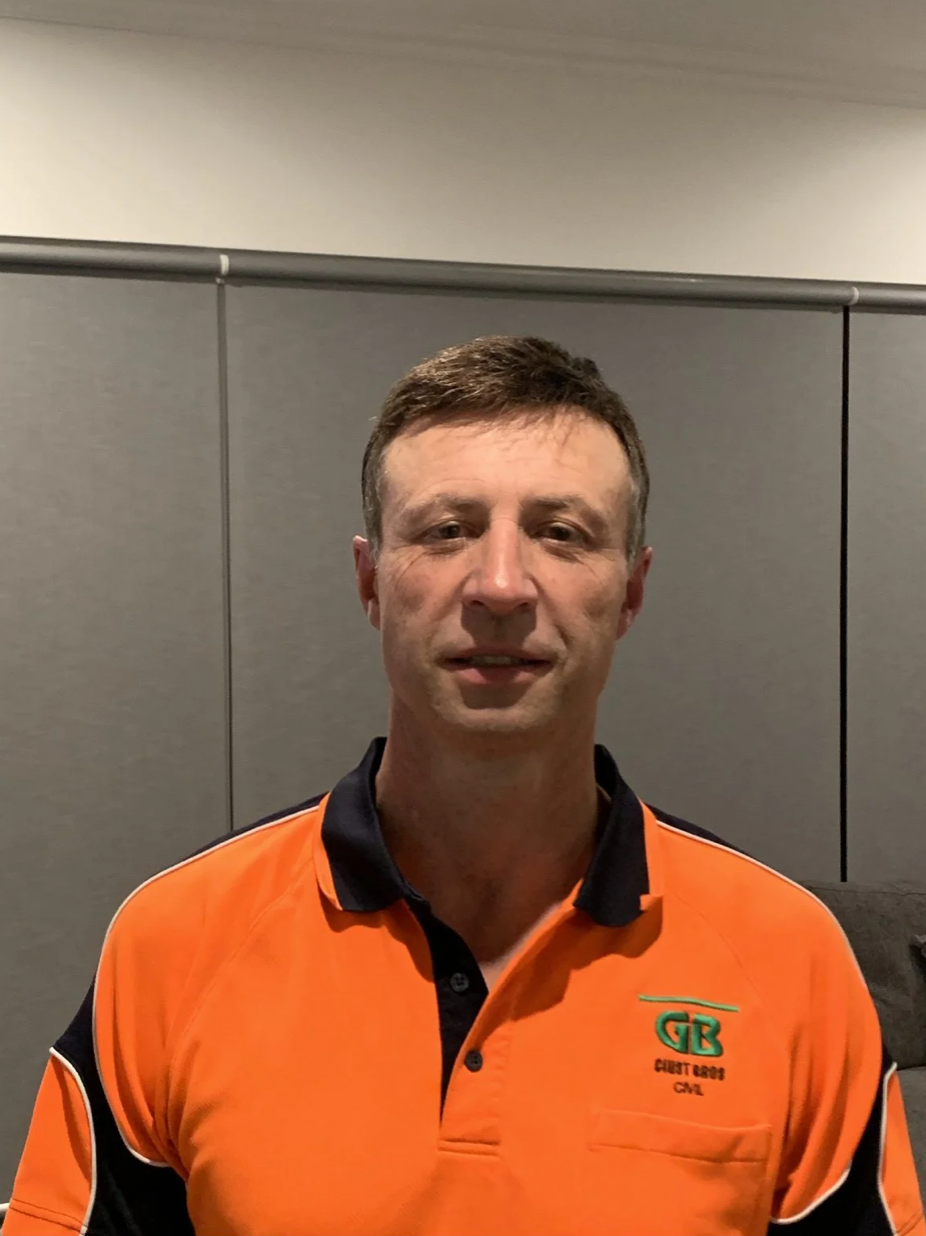 A man wearing an orange and black collared shirt with a logo that says "GB Guest Boards CAL" standing in front of a gray background.
