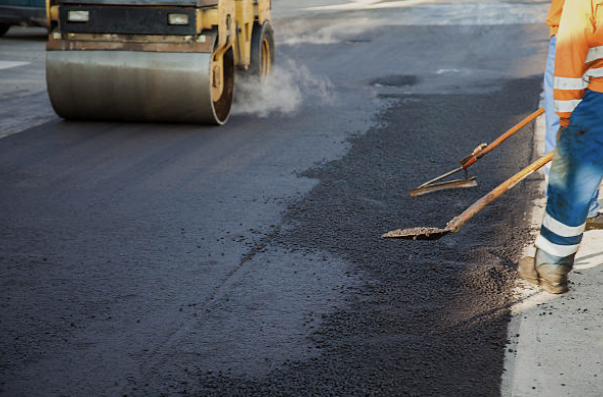 Workers in high-visibility clothing are laying asphalt on a road while a steamroller compacts it.