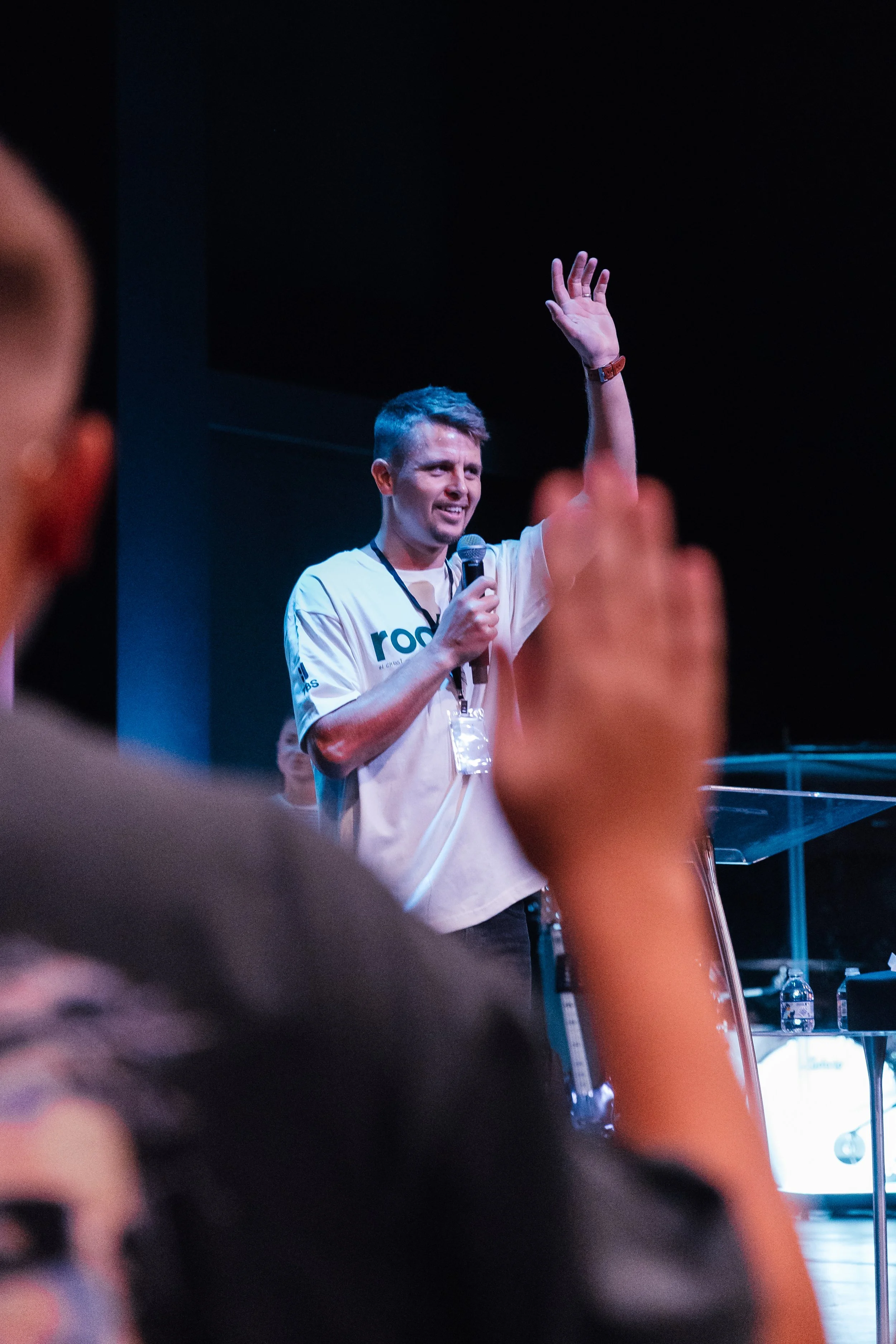 A young man holding a microphone and raising his hand on stage during a presentation or speech.