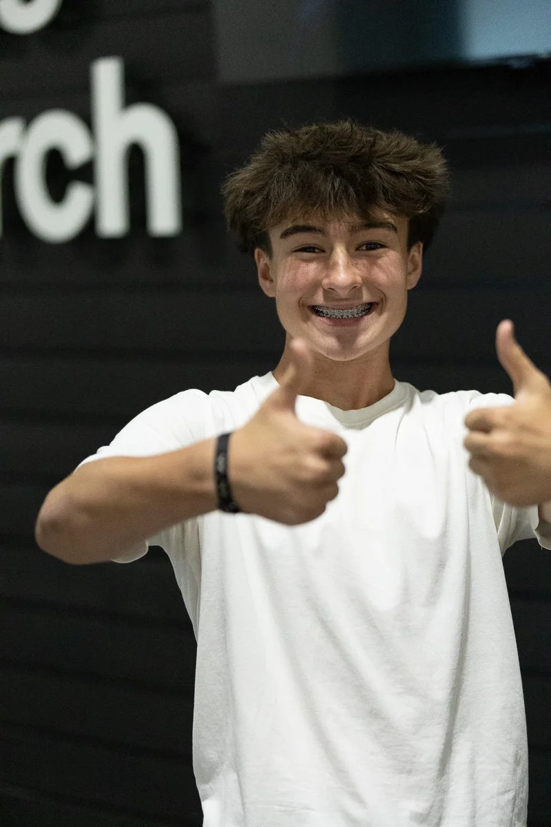 Young person smiling with braces, giving two thumbs up in front of a black background with white text.