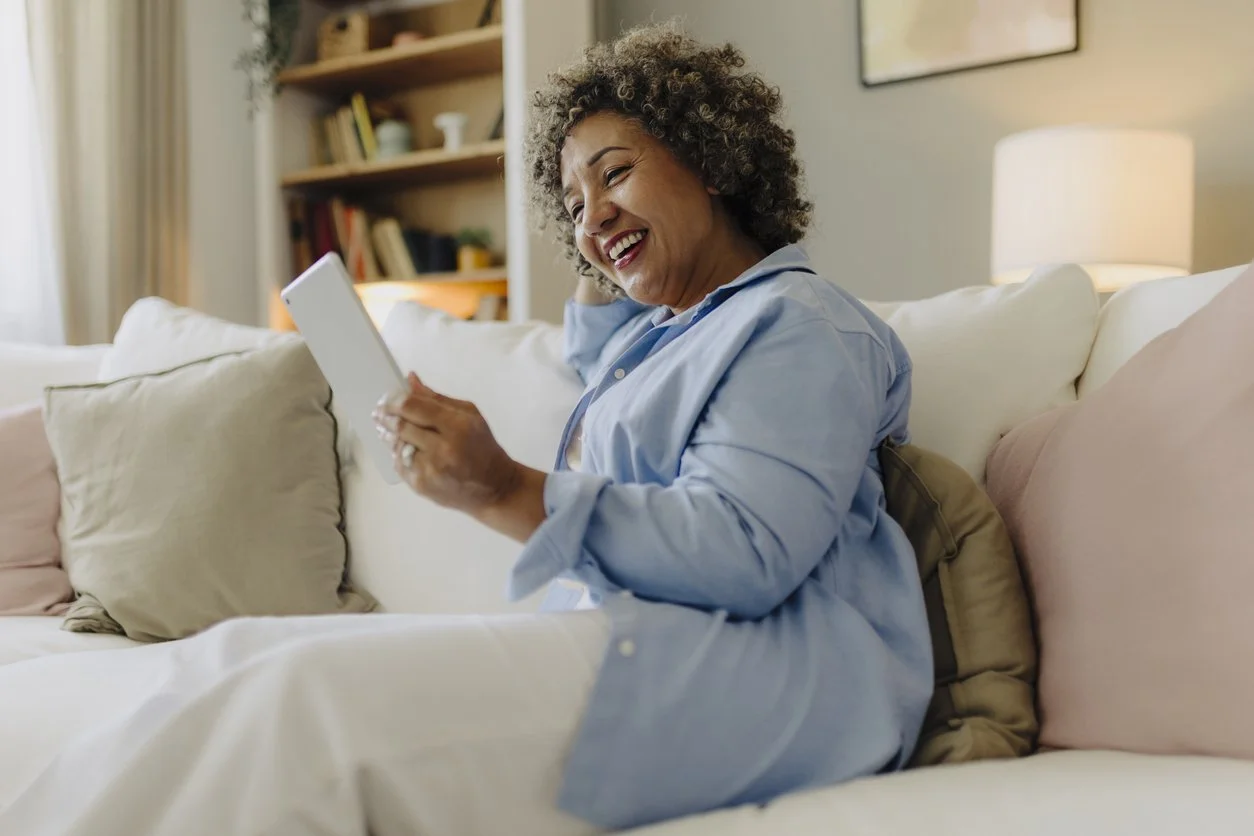 Woman holding phone and smiling while sitting on sofa
