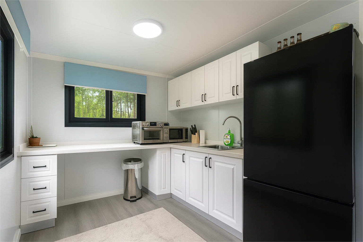 Modern kitchen with white cabinets, black refrigerator, window overlooking greenery, and countertop appliances.
