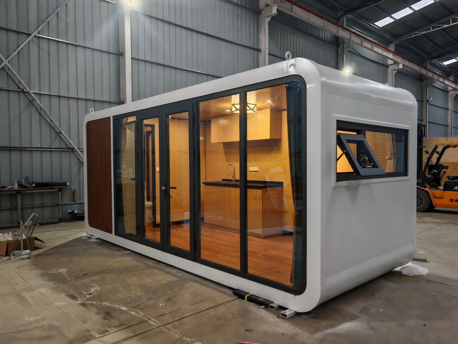 A compact modern tiny house with large glass sliding doors and a smaller window, situated in a warehouse or industrial building.