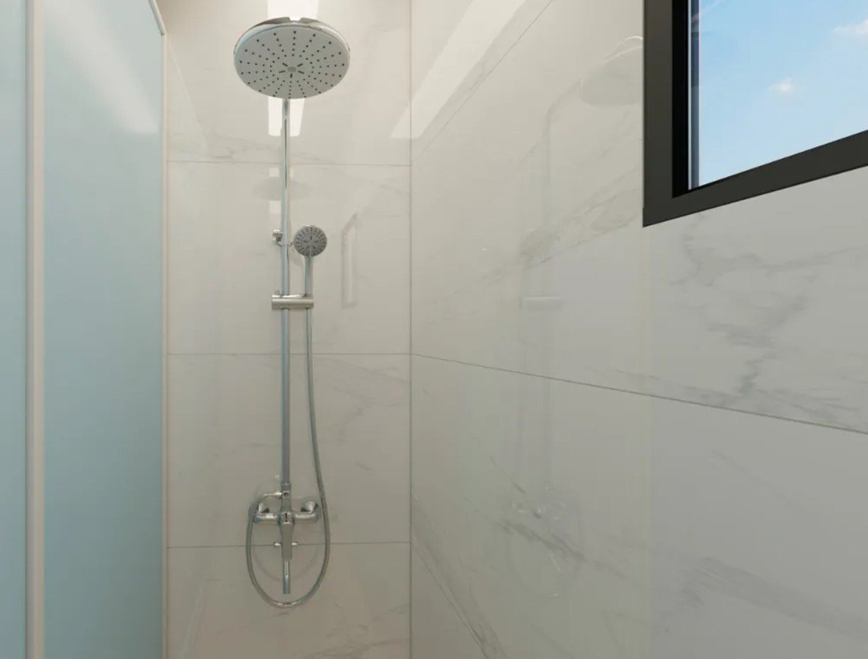 Modern shower with white marble wall tiles, a large overhead showerhead, a hand-held showerhead, and a window with a blue sky view.