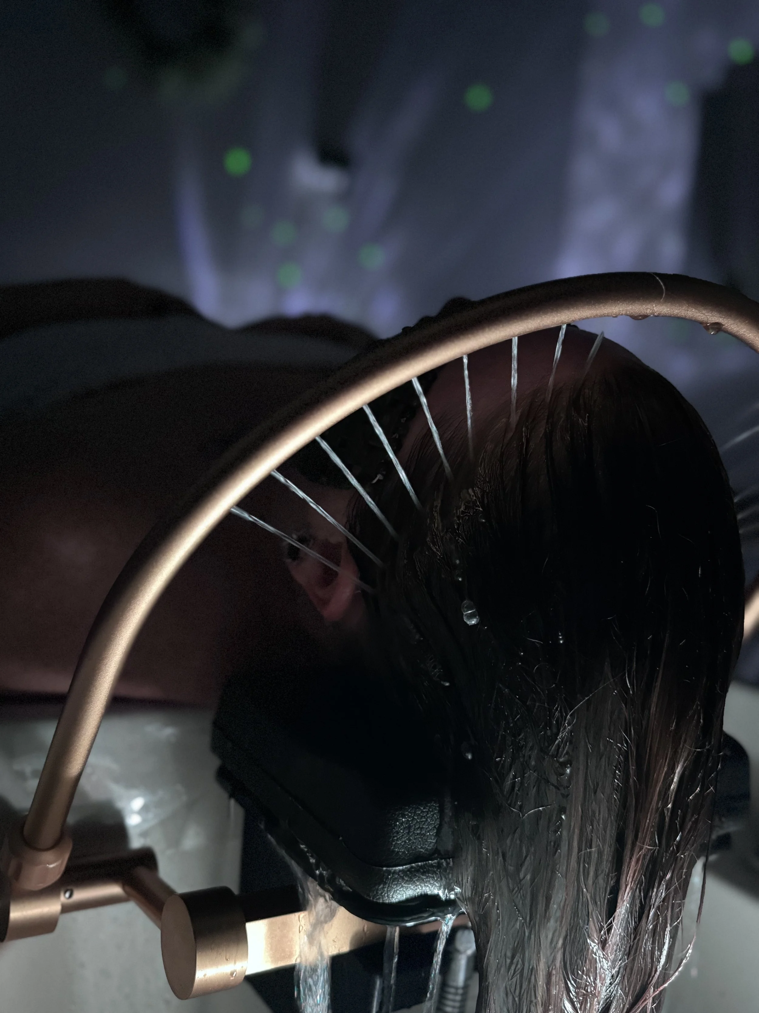 Close-up of a person reclining with an eye mask on, illuminated by exterior lights, while a metallic stand with a cylindrical knob is visible in the foreground.