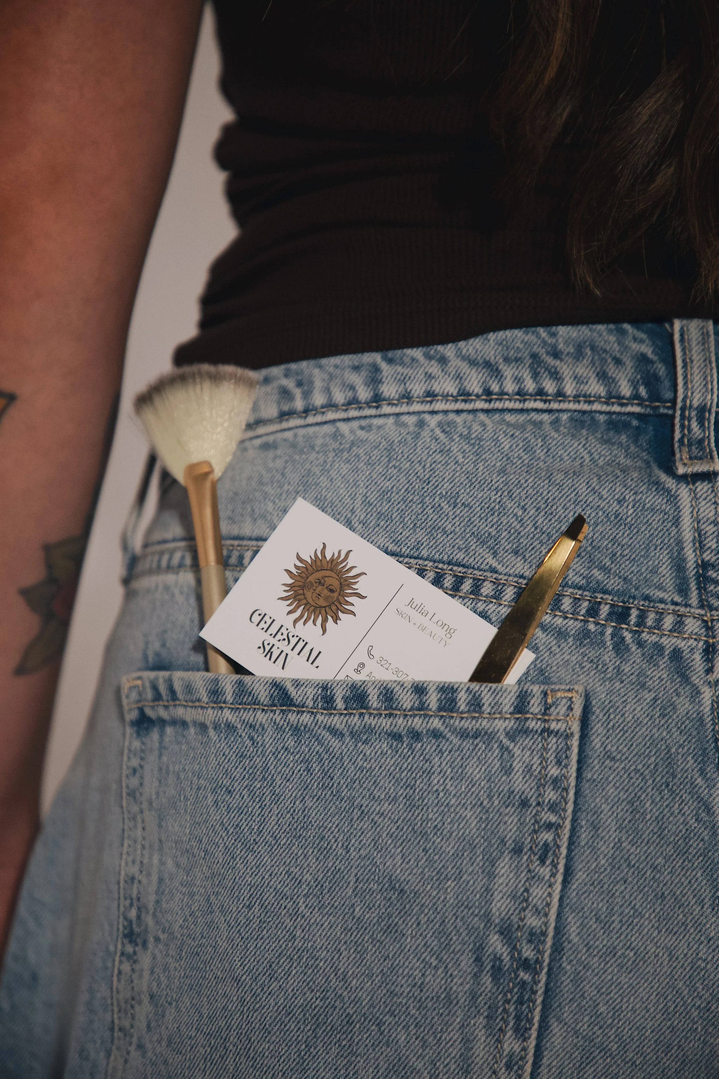 Close-up of a person's blue jeans with a business card and a makeup brush in the back pocket.