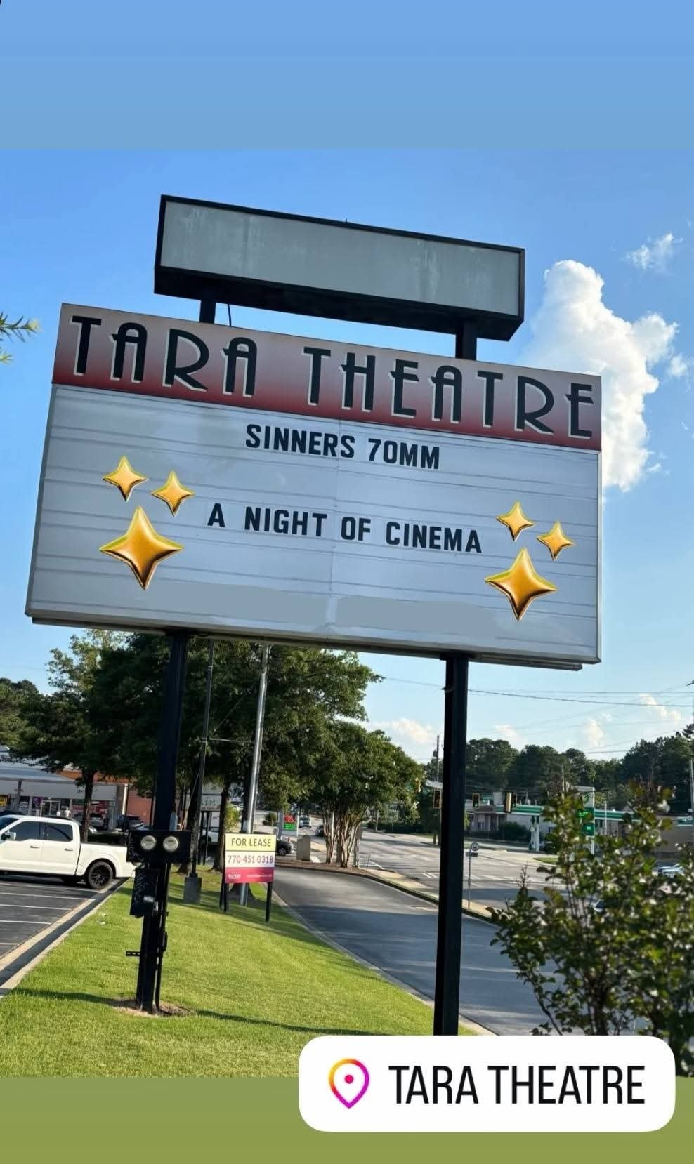 The Tara Theatre marquee sign advertising a film called "Sinners 70MM" and "A Night of Cinema" with decorative star graphics, against a background of a sunny sky and trees.