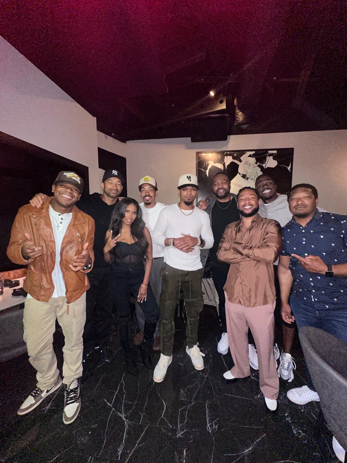 A group of nine people standing together indoors, smiling and posing for the photo.