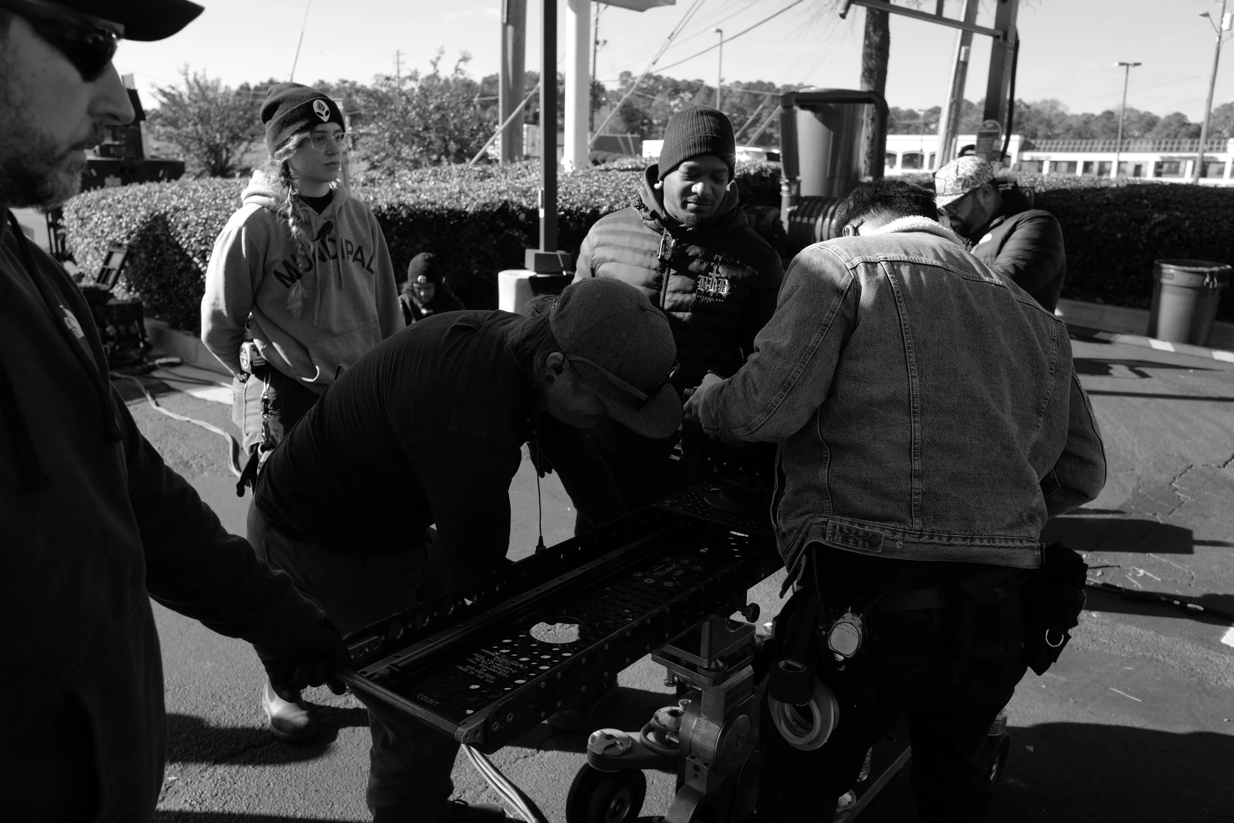 Group of people working together on a film or video project outdoors, with some adjusting equipment on a cart.