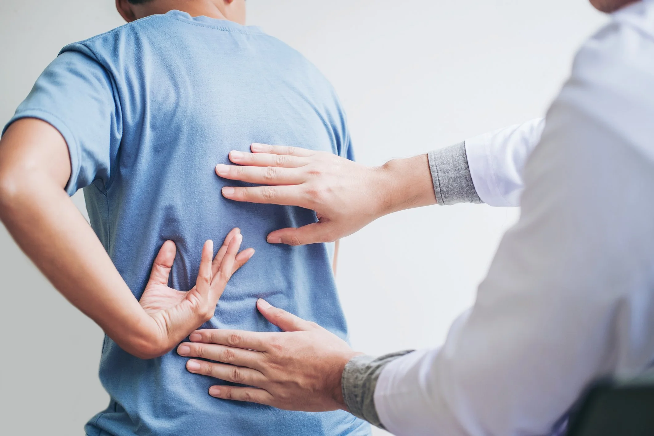 Medical professional examining back pain in a patient using hands and palpation.