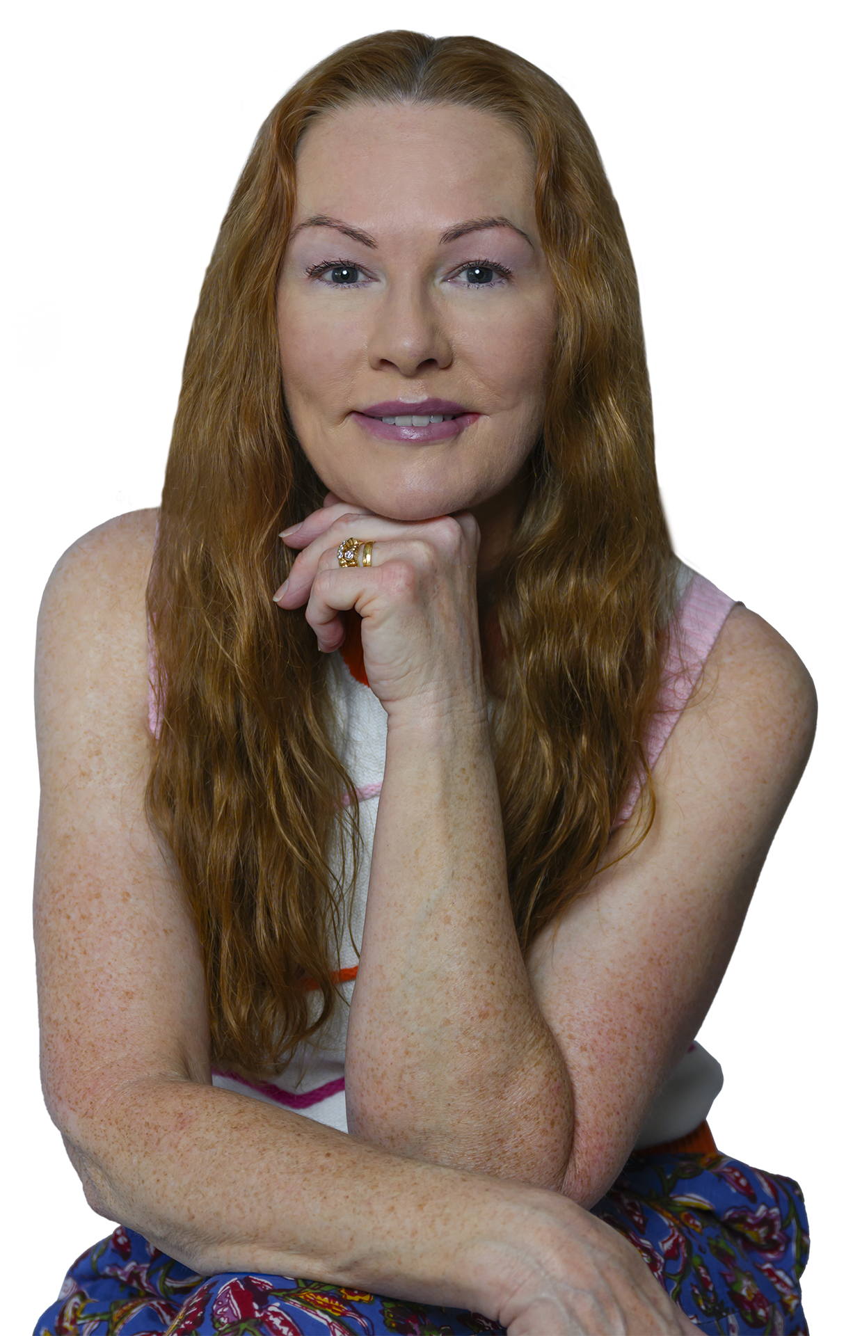 A woman with long red hair, blue eyes, and freckles, resting her chin on her hand and smiling gently at the camera.