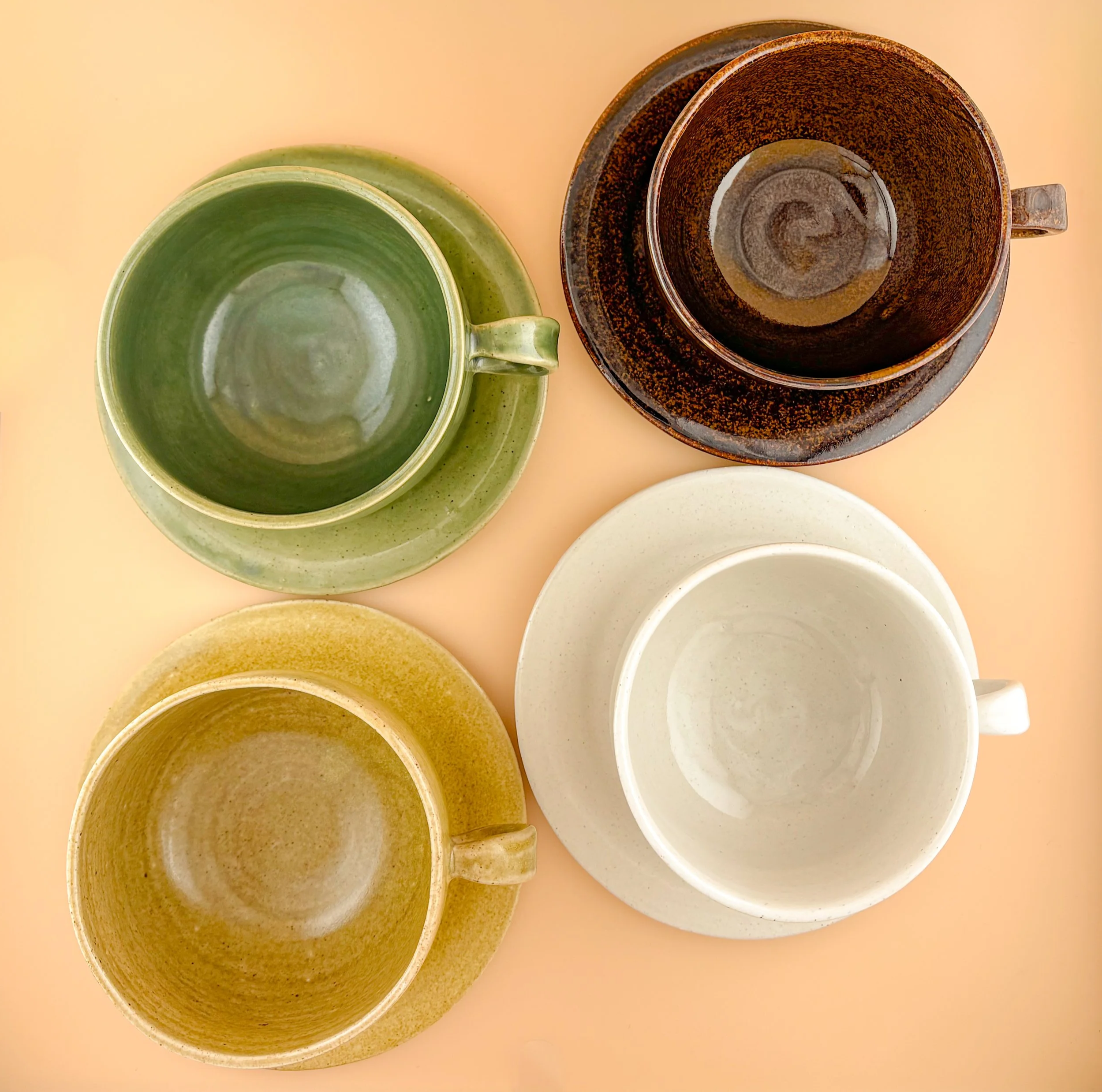 Top-down view of ceramic matcha mugs and saucers in Rituals colors: jade, dark roast, first light, golden hour.
