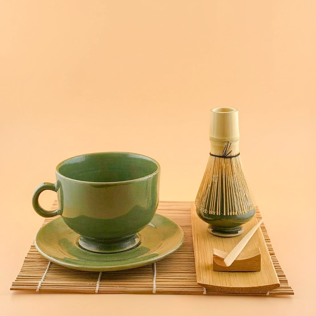 Handmade ceramic matcha mug and saucer in Ceremonial Jade styled with matcha whisk stand on bamboo mat.