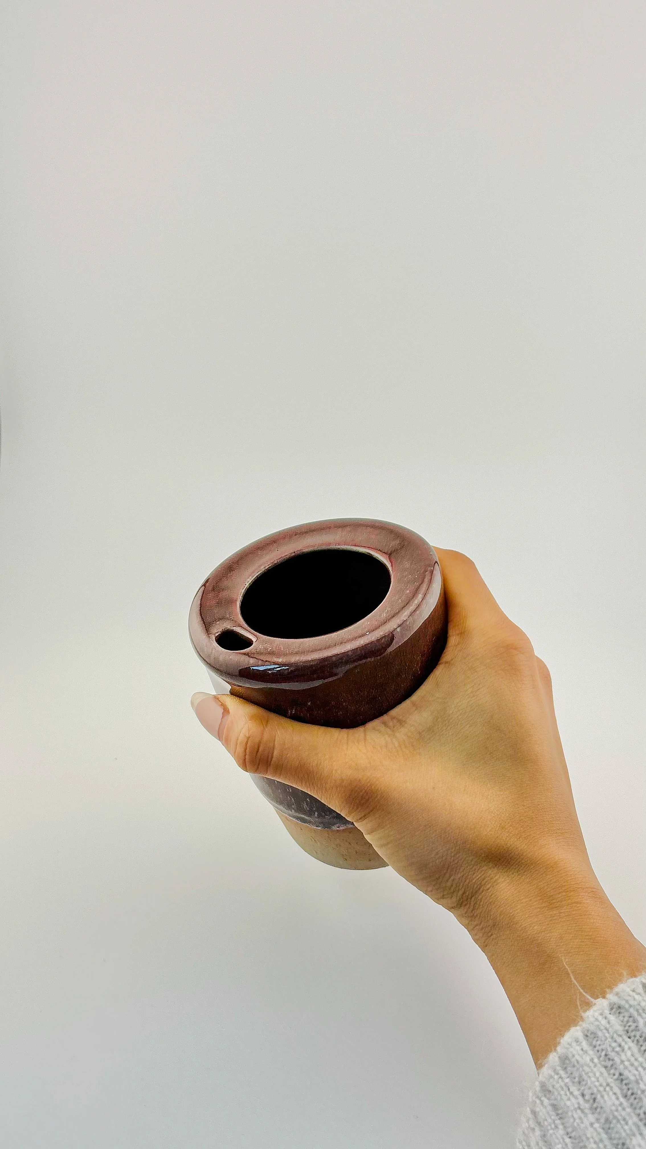 Hand-thrown ceramic travel mug held in hand from above showing flanged lid-free rim design, burgundy reduction glaze, artisan stoneware travel cup.JPG
