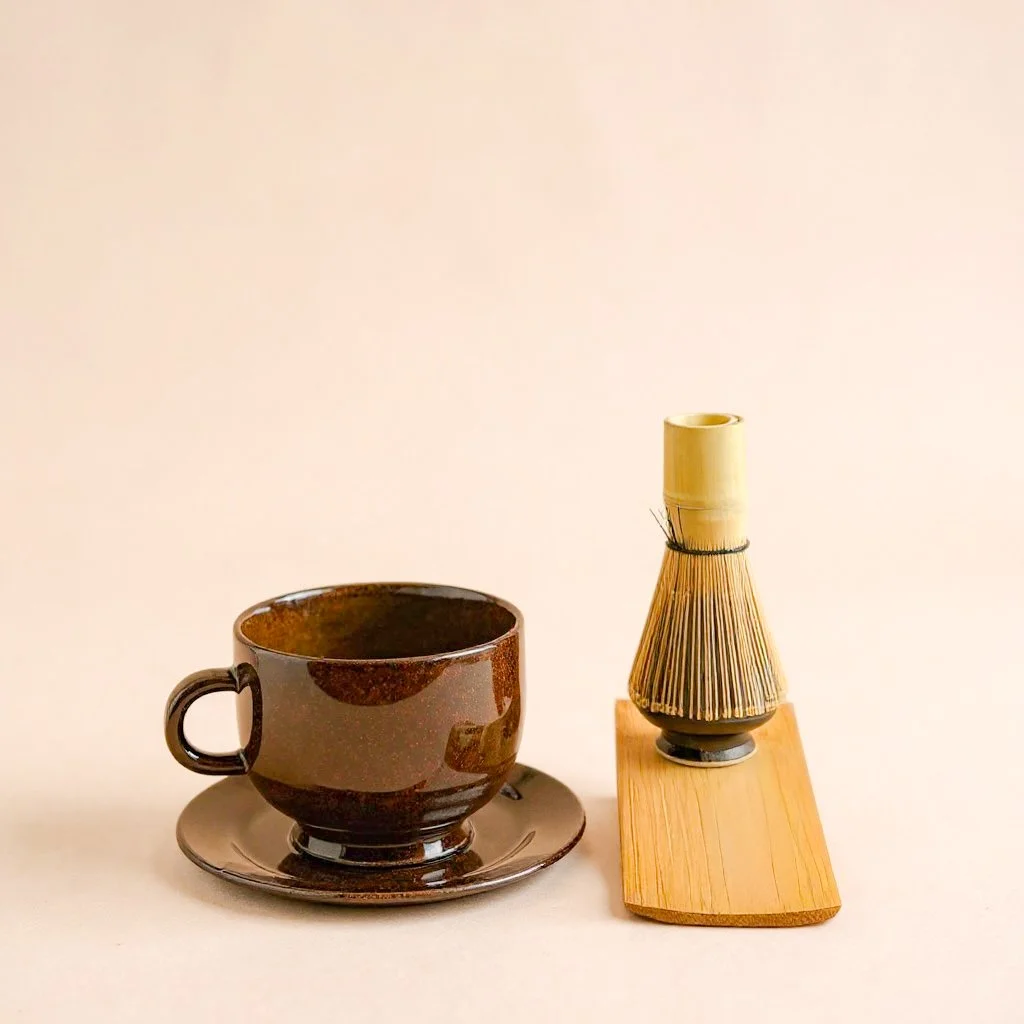 Dark Roast ceramic matcha mug and saucer styled with matcha whisk stand for ritual setting; listing includes mug and saucer only.