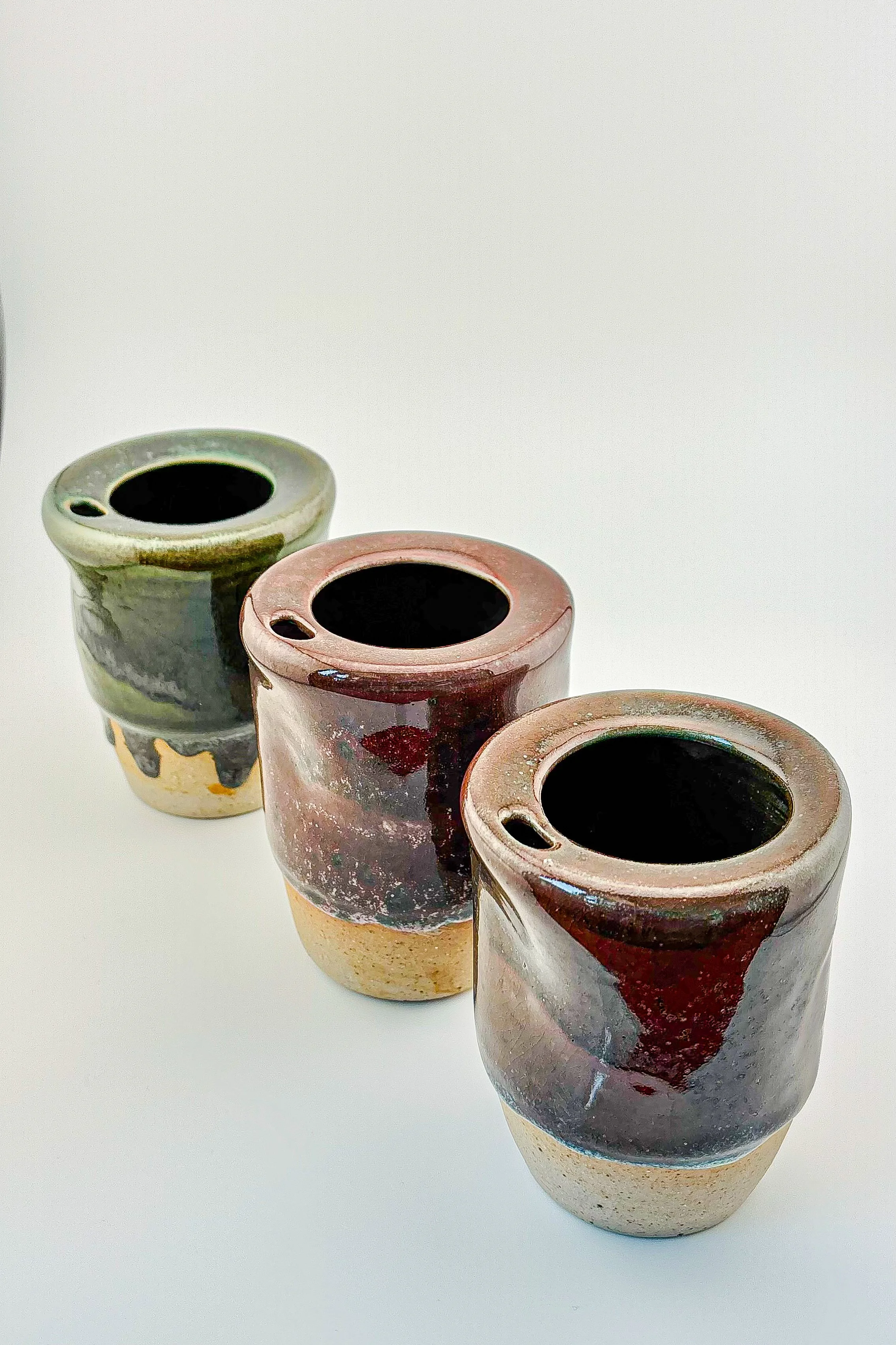 three+handmade+ceramic+travel+cups+grouped+together+showing+size+and+scale%2C+mixed+reduction+glazes+in+burgundy+and+mauve%2C+artisan+stoneware+pottery+collection.png