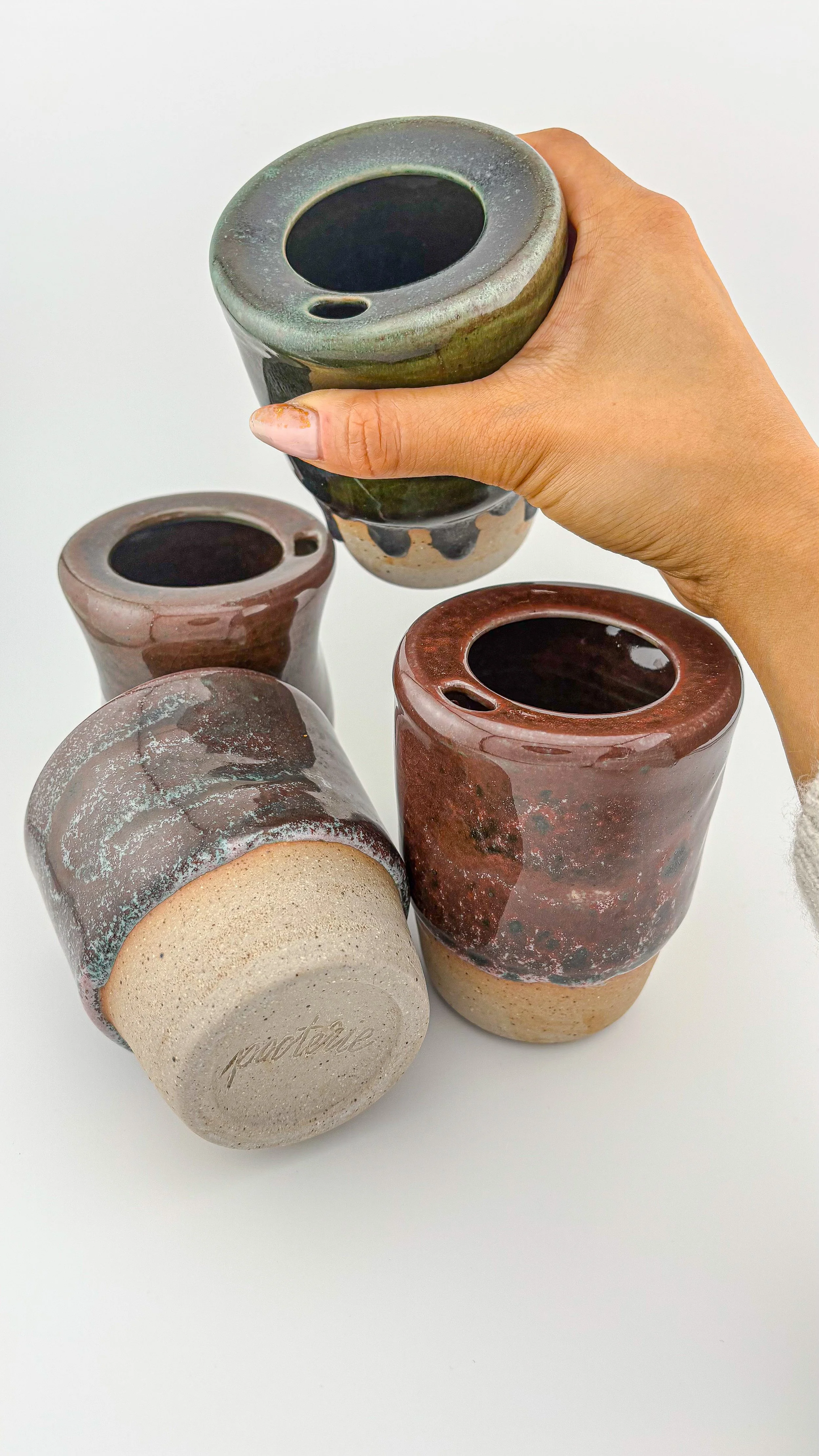 Collection of handmade reduction-fired ceramic travel cups in burgundy and mauve glaze tones, artisan stoneware pottery.JPG
