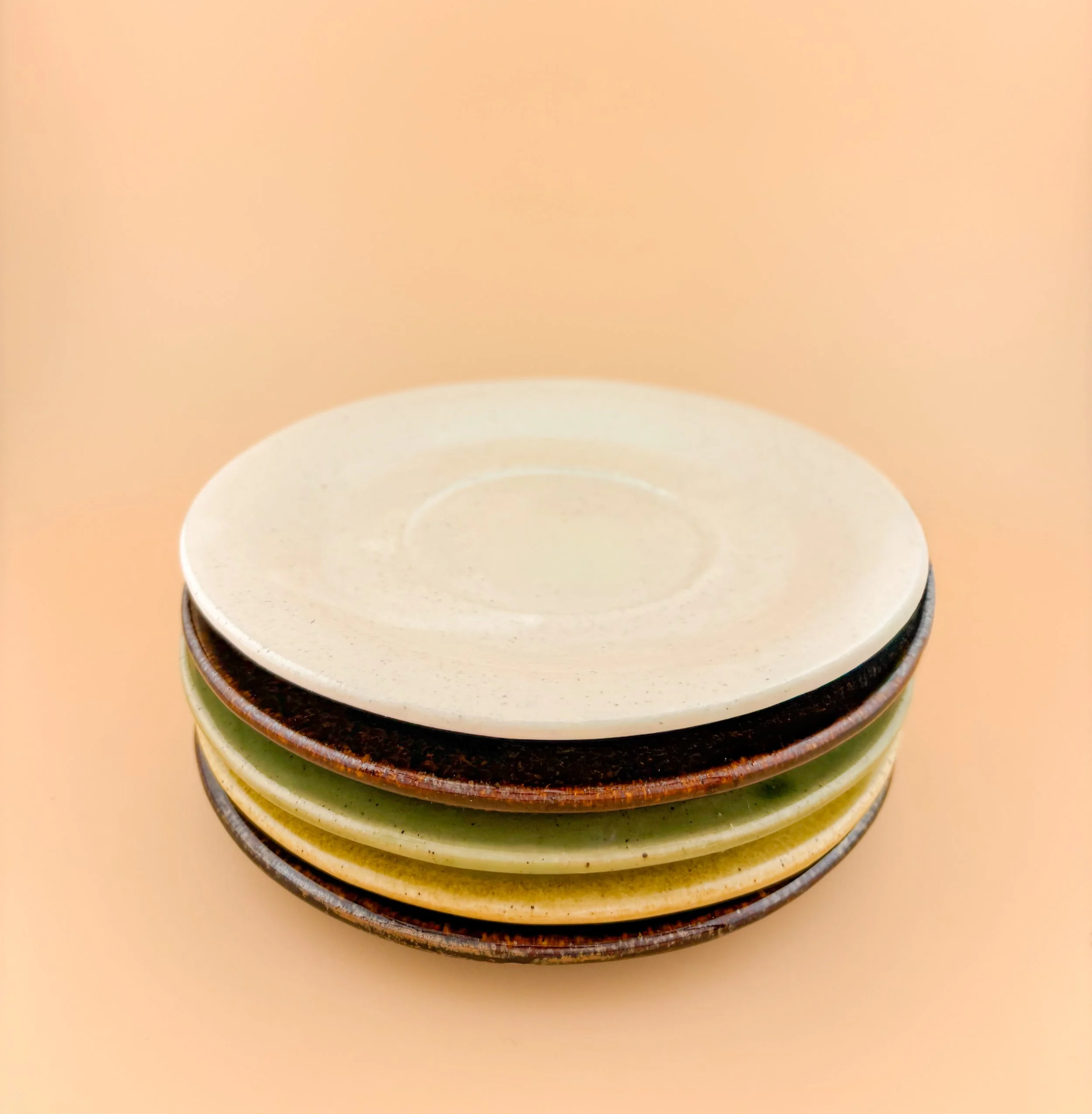 Stack of handmade ceramic multi-use saucers in Rituals colors, wheel-thrown stoneware.