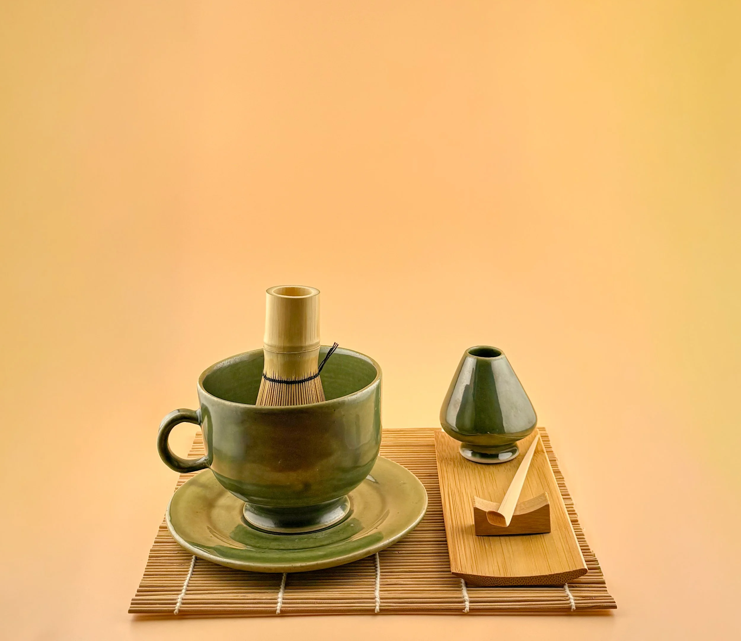 Handmade ceramic matcha set in Ceremonial Jade, featuring matcha mug, multi-use saucer, and matcha whisk stand on bamboo mat.