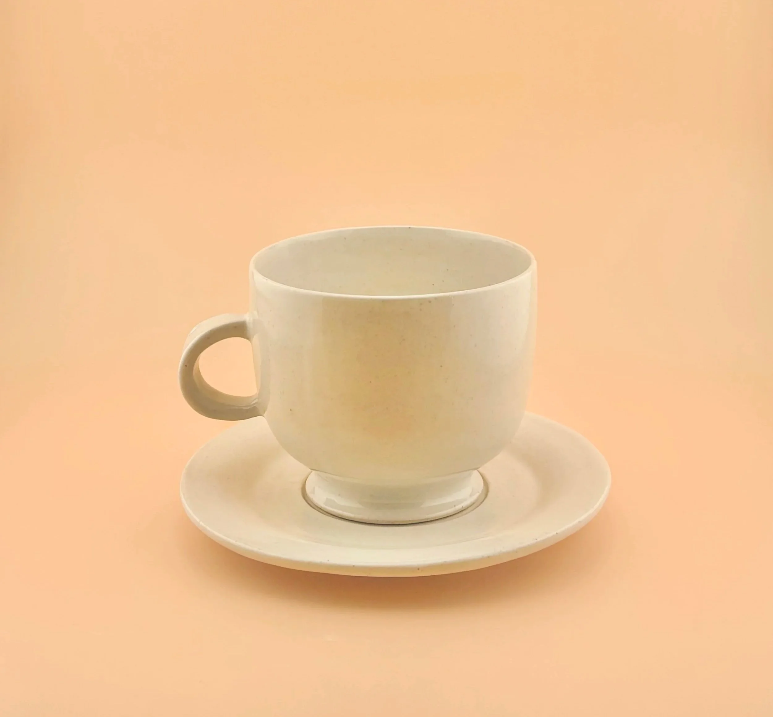 White ceramic matcha mug resting on its matching multi-use saucer against a warm peach background.