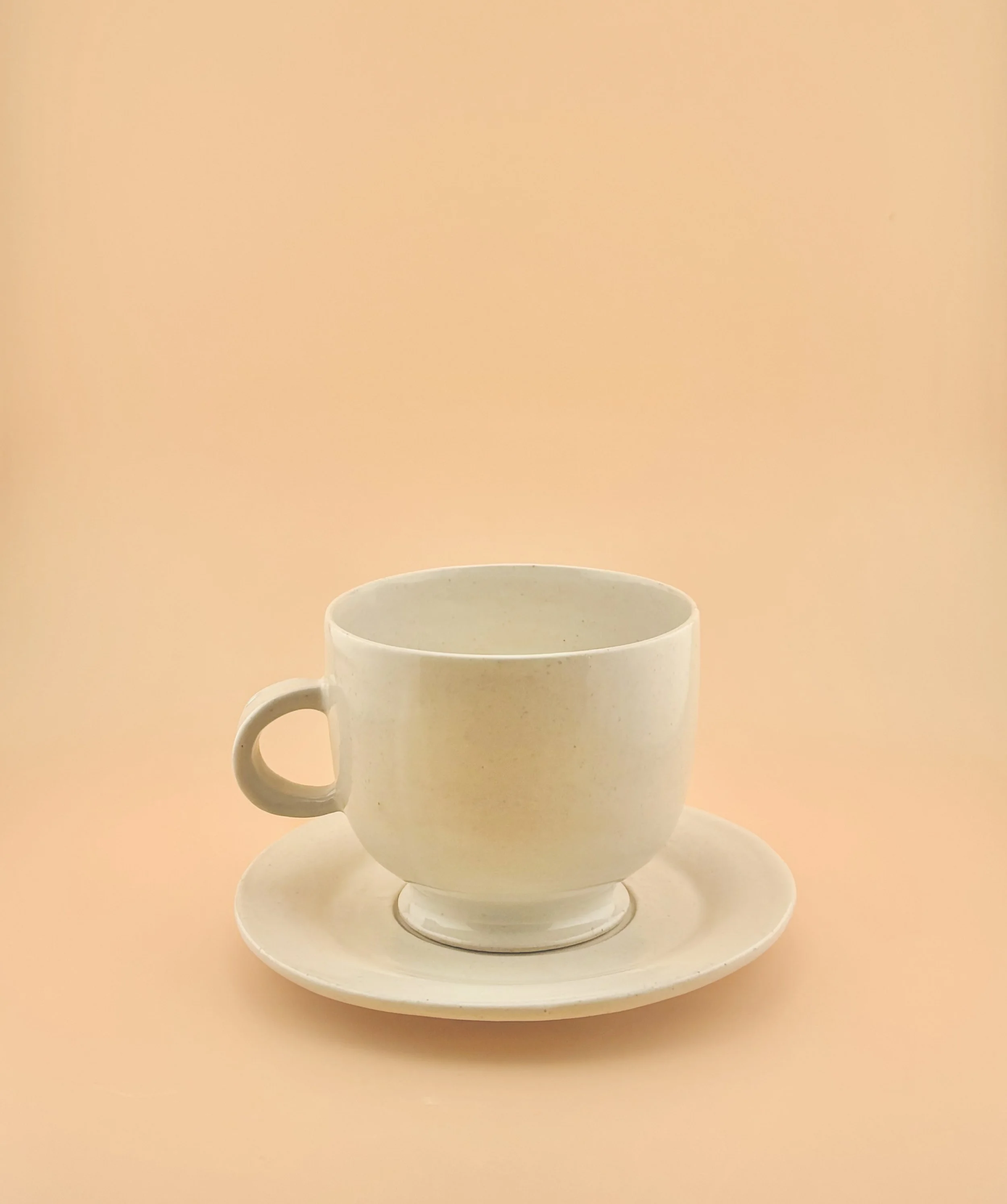 White ceramic matcha mug on matching saucer against warm peach background.