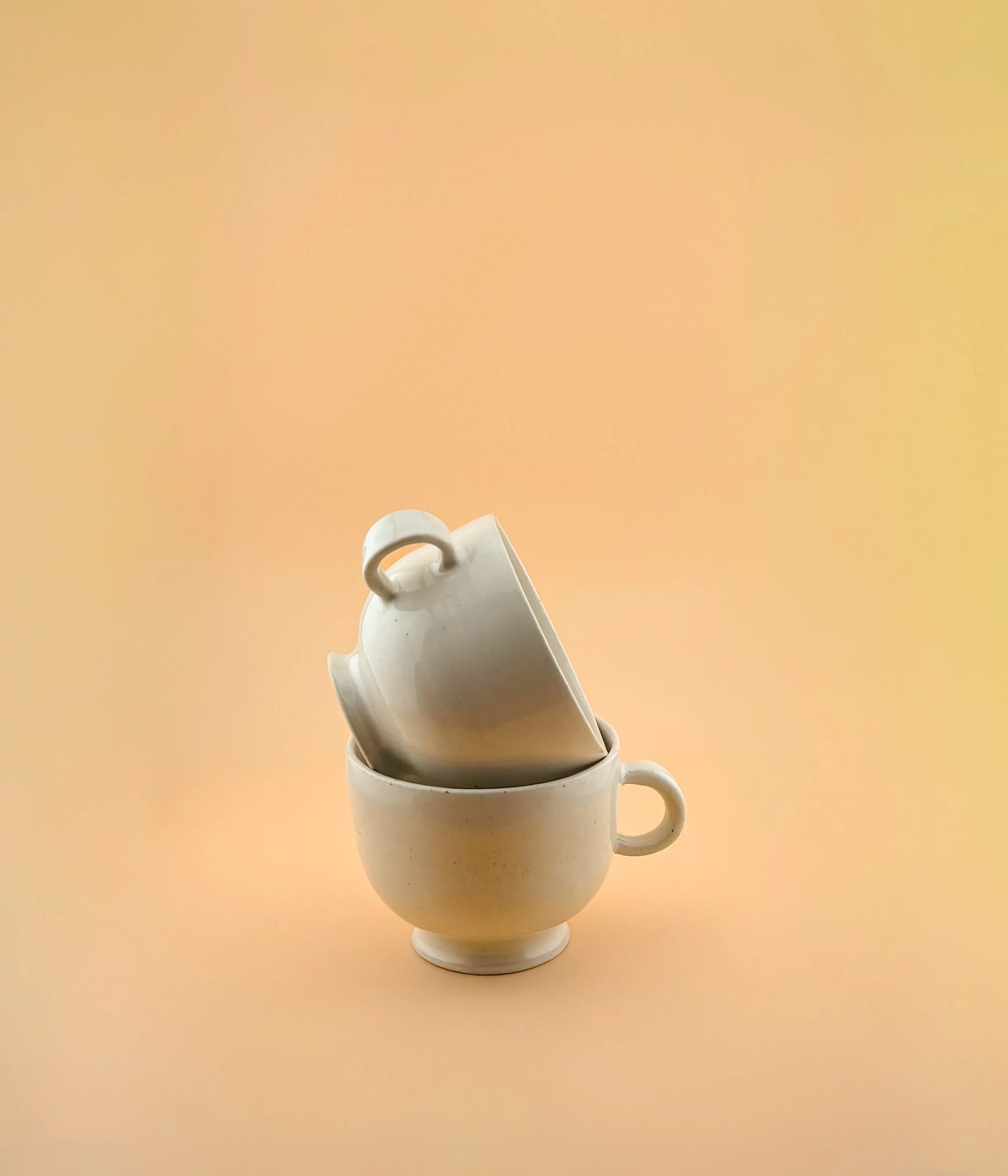 Stacked ceramic matcha mugs showing handle design and glaze colors on peach background.