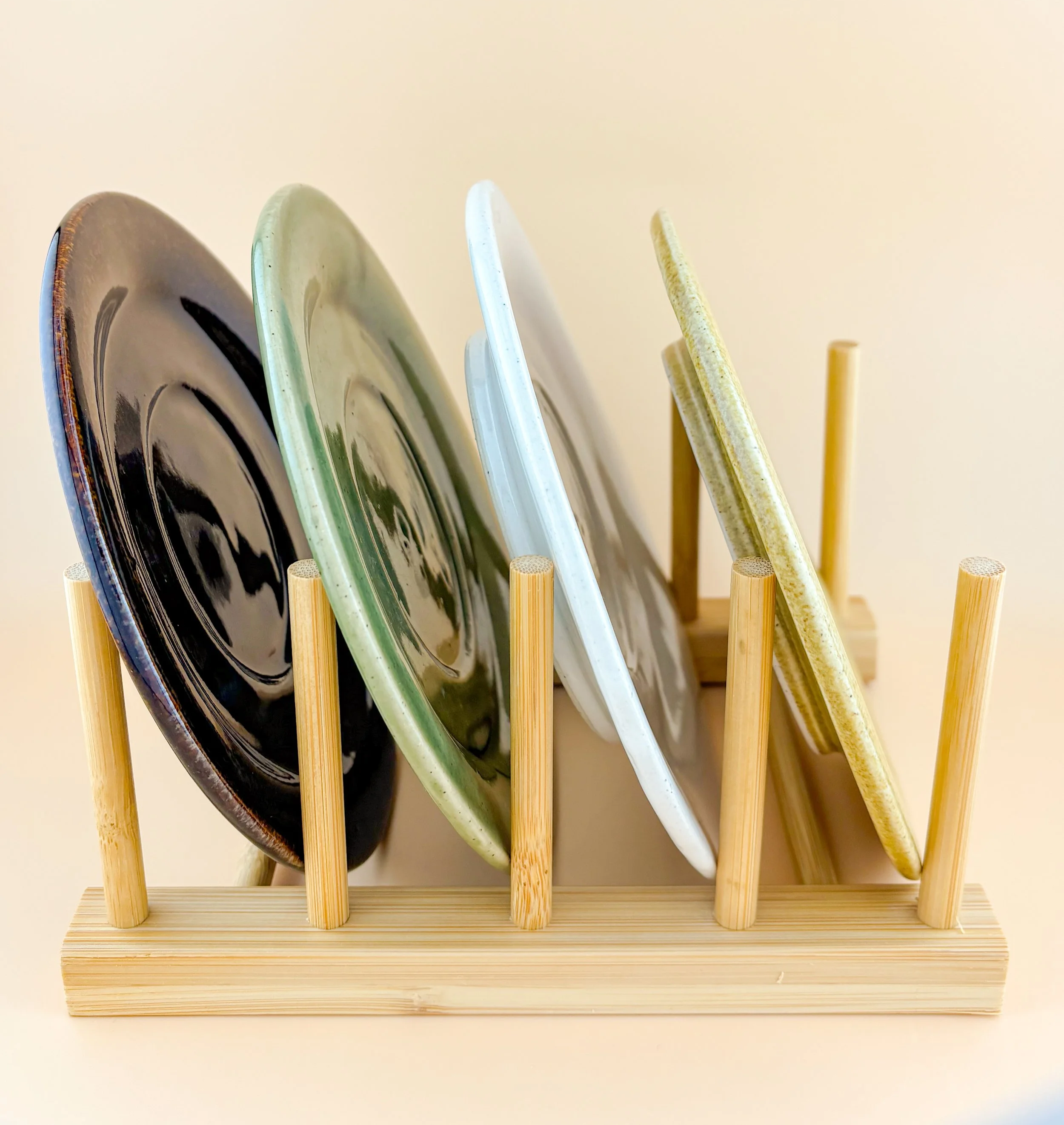 Side view of handmade ceramic saucers in multiple Rituals colors stored vertically in a wooden dish rack.