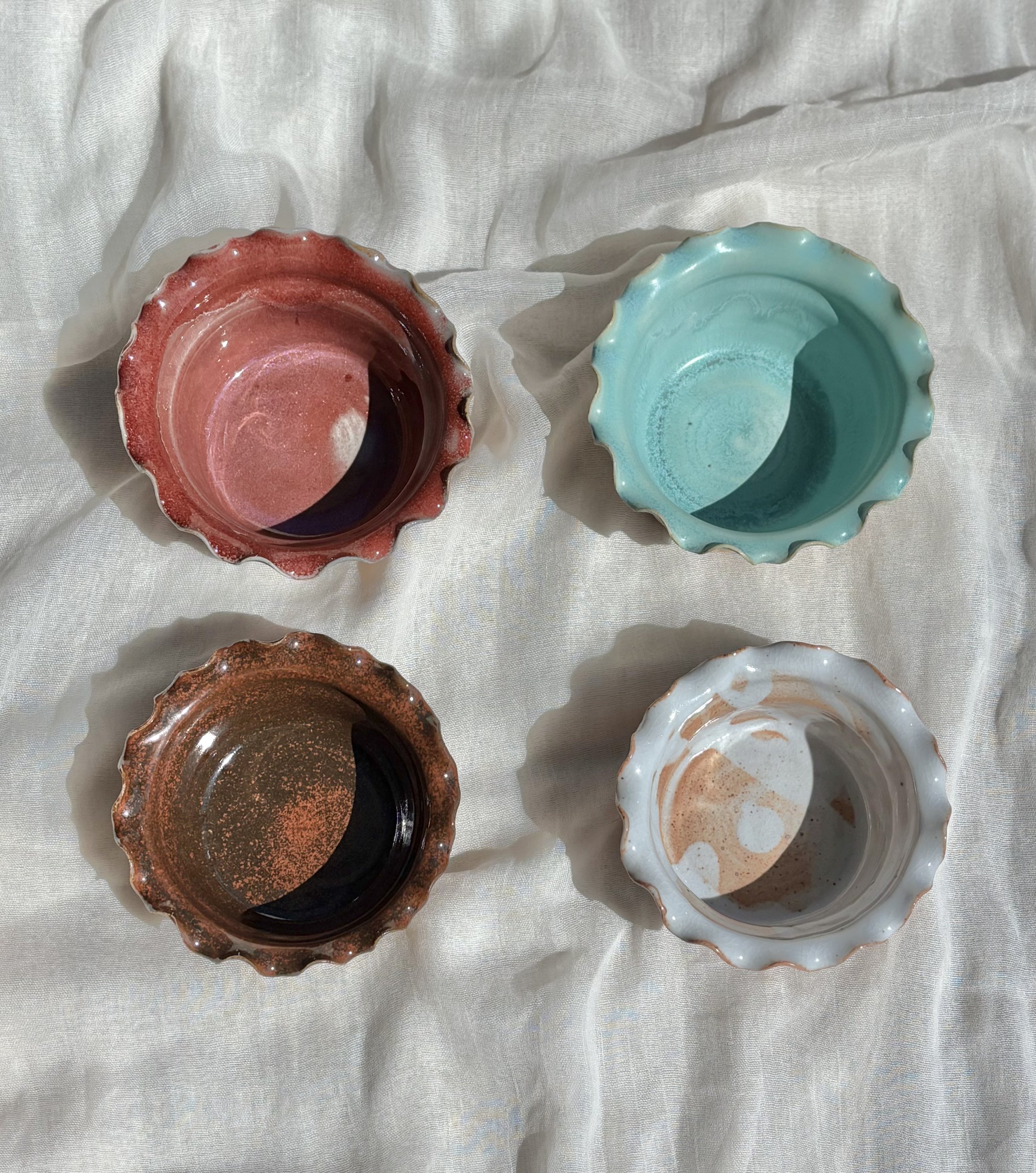 Four handmade ceramic ice cream bowls in strawberry, mint, chocolate brownie, and salted caramel arranged on white fabric.jpg