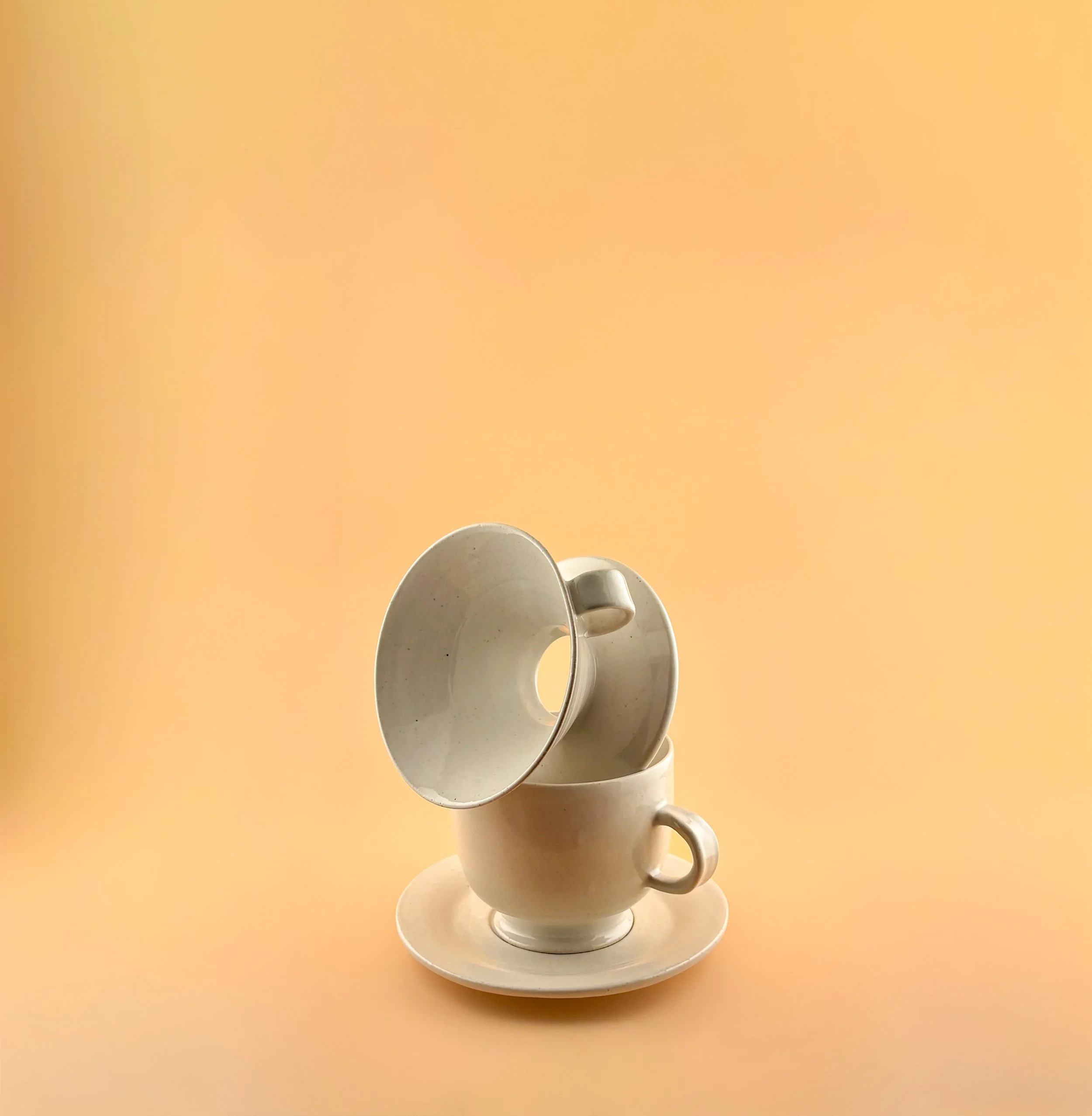 Ceramic pour-over coffee dripper tilted above matching mug and saucer, demonstrating fit and function in the Rituals Collection.