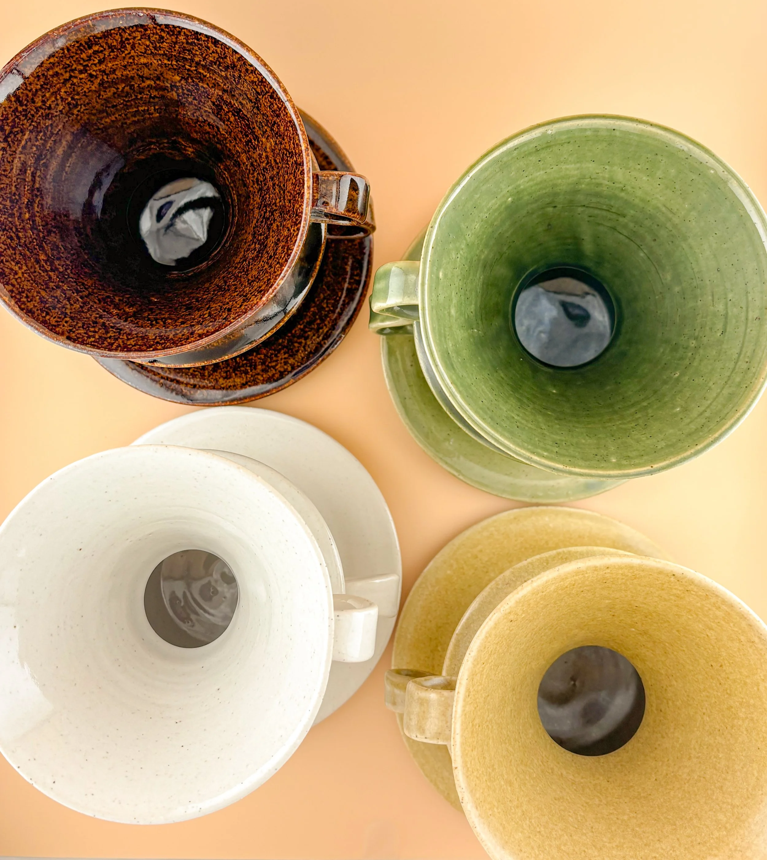 Top-down view of handmade ceramic pour-over drippers in Dark Roast, Jade, First Light, and Golden Hour glazes, showing interior glaze variations.