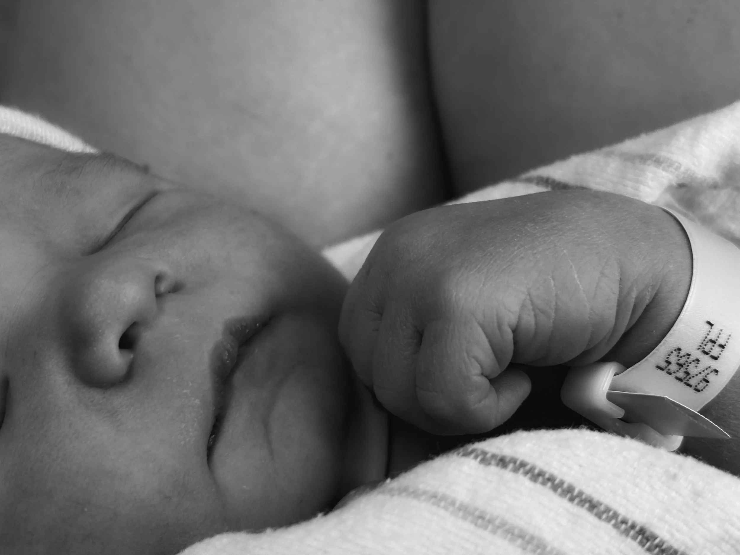 Close-up of a sleeping newborn baby with a hospital identification bracelet on their wrist.
