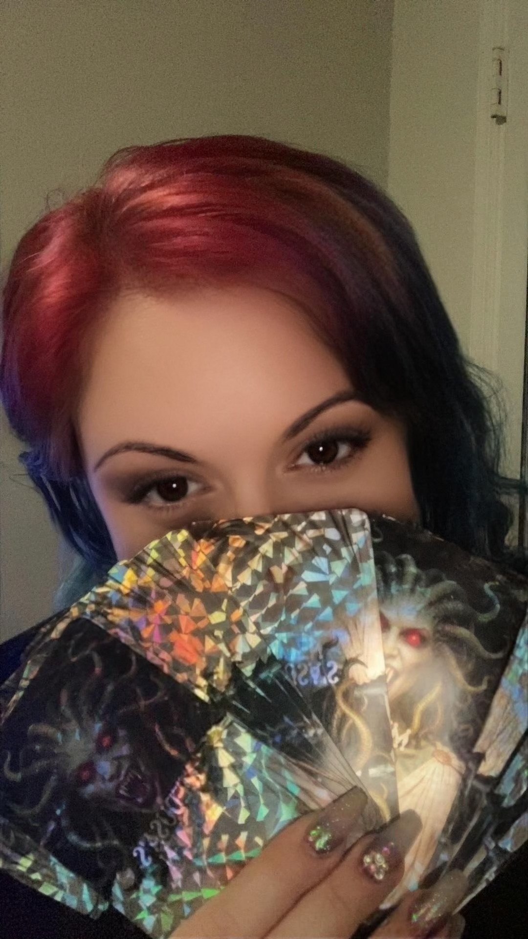 A woman with multicolored hair holding a decorative fan featuring a mythical creature with red eyes.