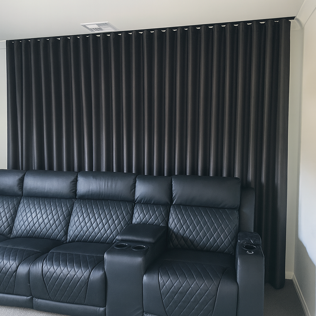 Black leather theater-style seating with diamond stitching and built-in cup holders, set against a black curtain wall.