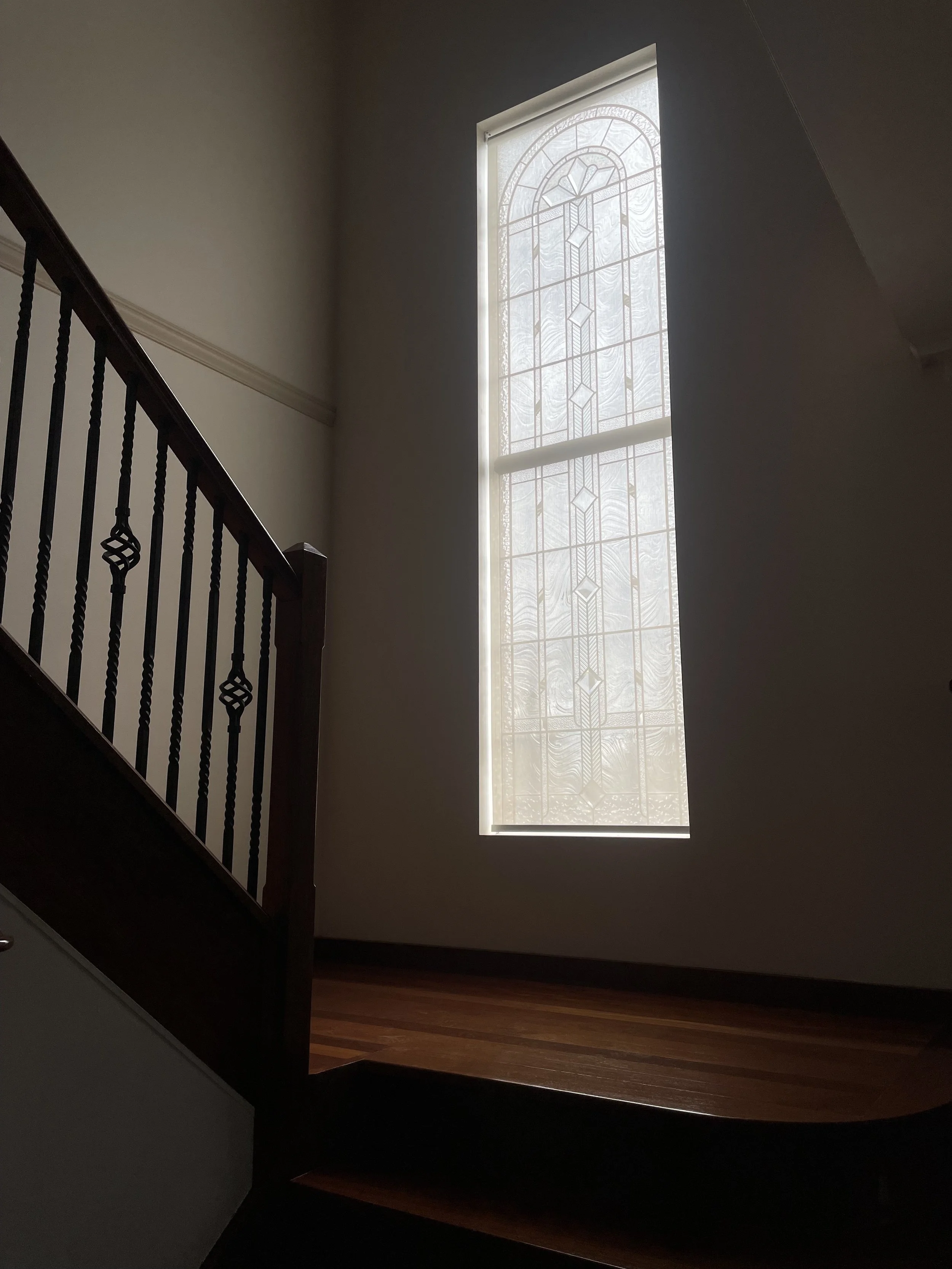 Interior view of a staircase with dark wood banister and spindles, facing a tall stained glass window that lets in natural light.
