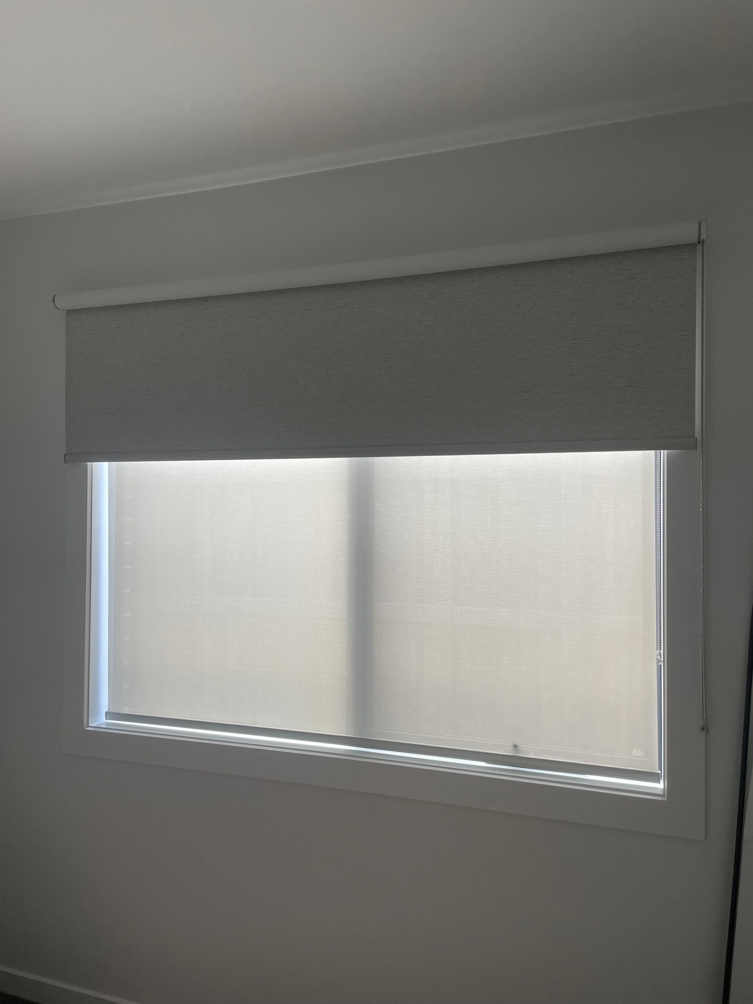A window with a gray roller shade partially pulled down, allowing some light to enter the room.