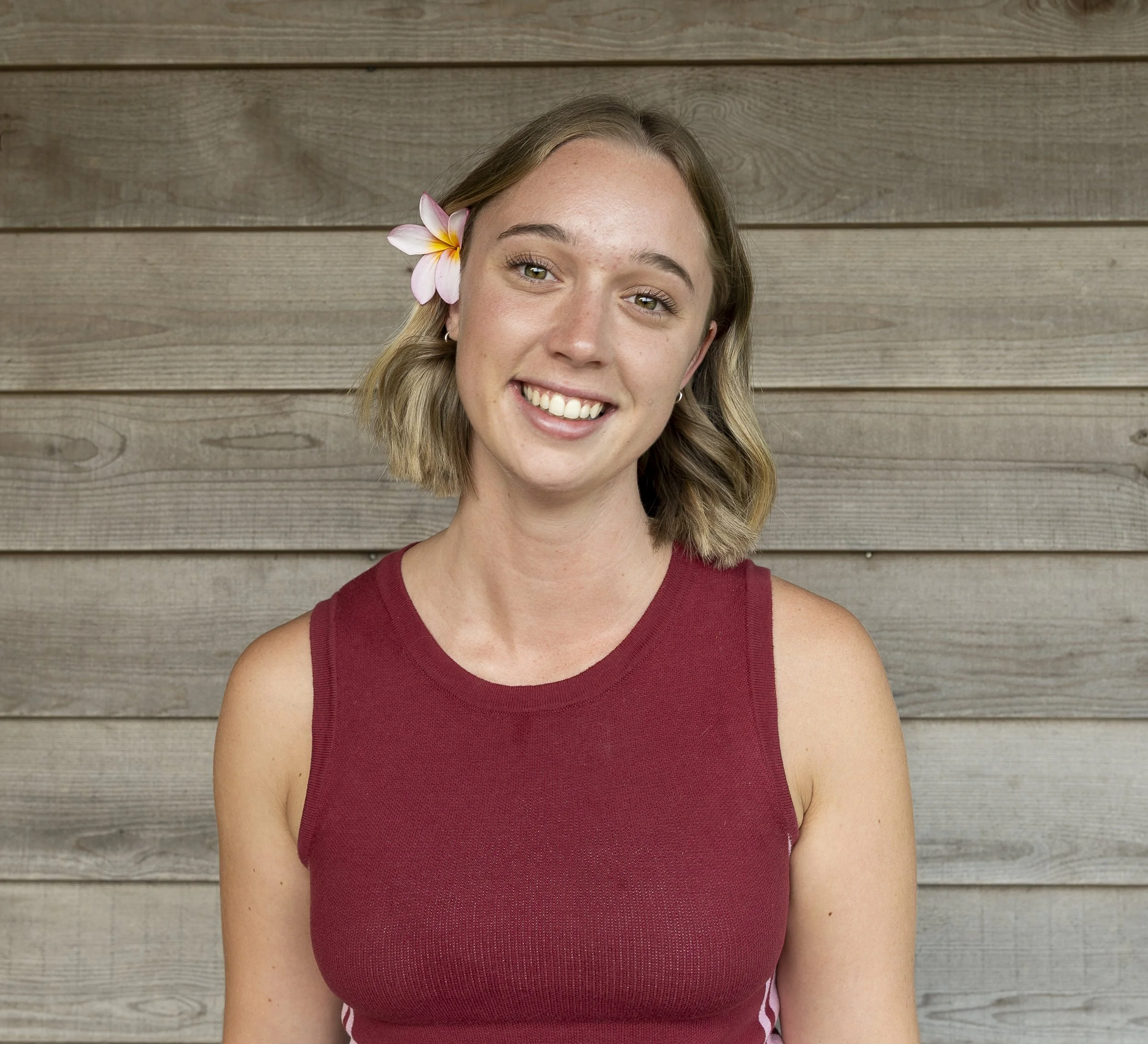 A woman with shoulder-length blonde hair, wearing an olive green turtleneck sweater, sitting against a background of wooden paneling.