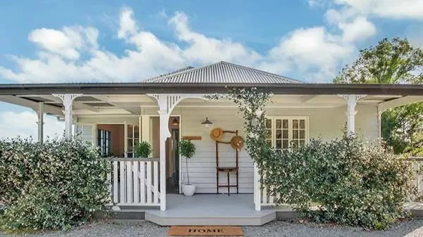 Front view of a cozy white house with a porch, decorated with plants, and a welcome mat that says 'Home.'