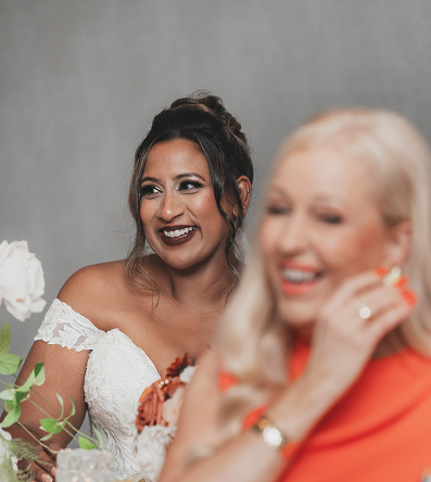 A woman in a white wedding dress smiling, with a blurred woman in a red dress beside her.