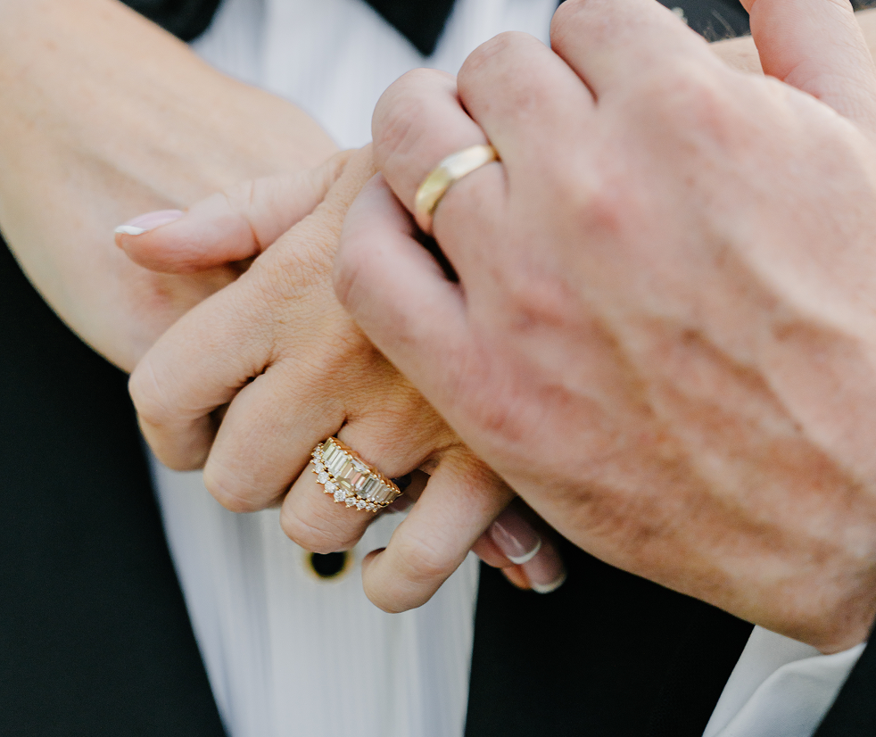 Close-up of intertwined hands wearing wedding rings, one with a diamond-studded ring, suggesting a marriage or engagement.