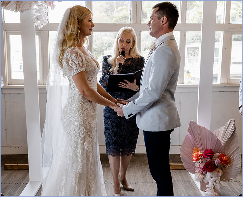 A bride and groom exchange wedding vows holding hands during a wedding ceremony indoors with an officiant in the background.