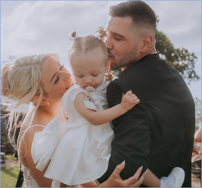 A family of three celebrating outdoors, with the mother and father holding their young daughter.