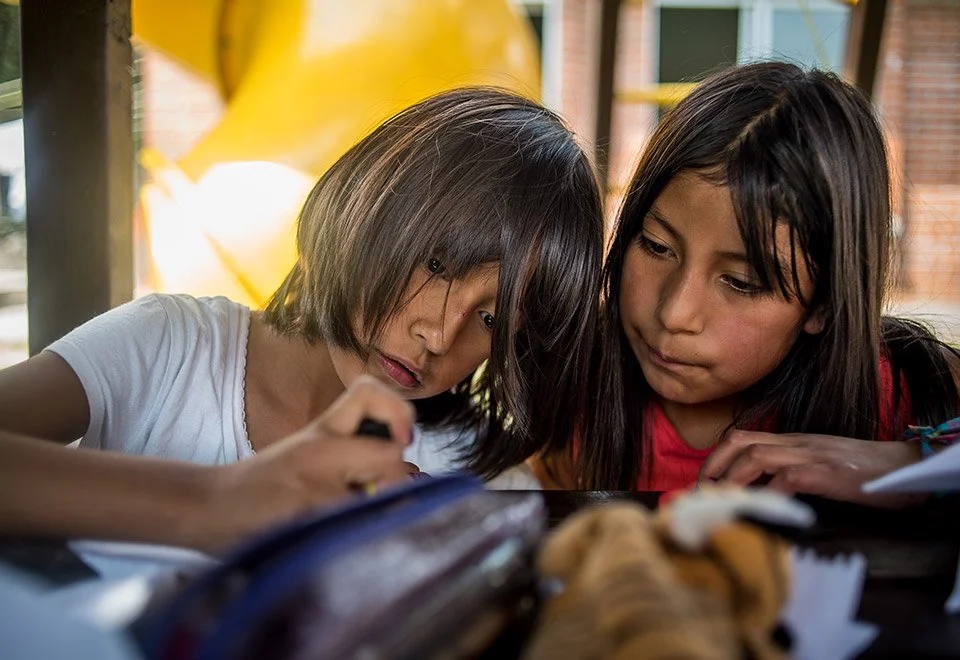 Dos niñas observando un objeto en una mesa, una de ellas sosteniéndolo con una mano.