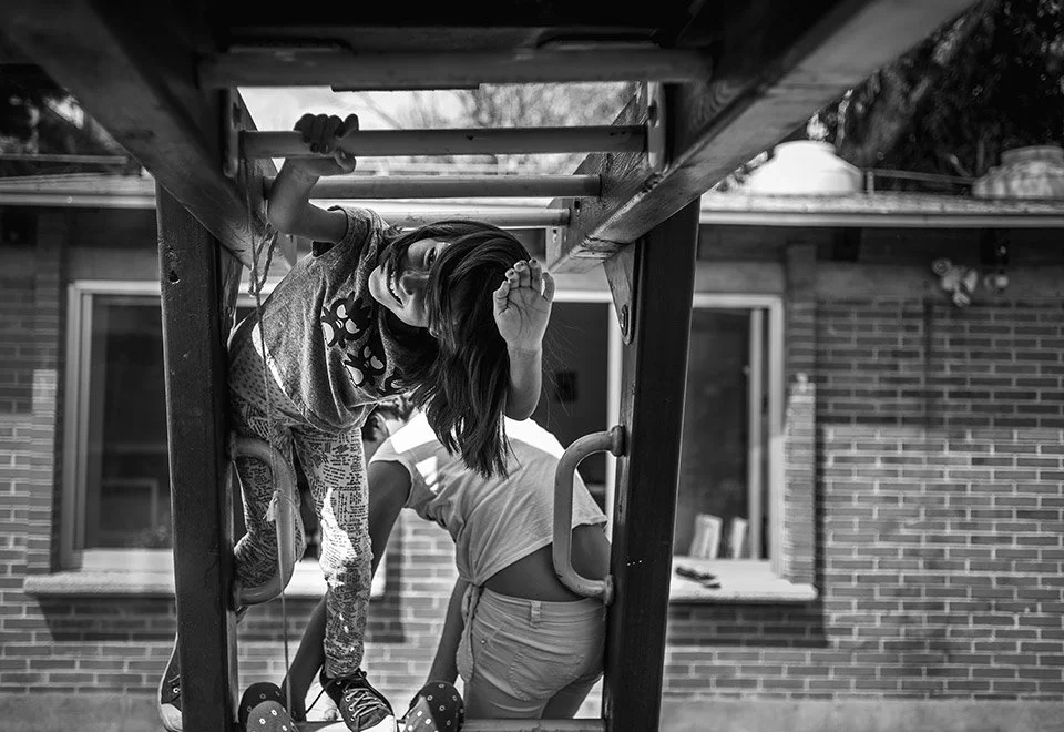 Niña jugando en un juego de parque infantil en un fondo de casa de ladrillos, en blanco y negro.