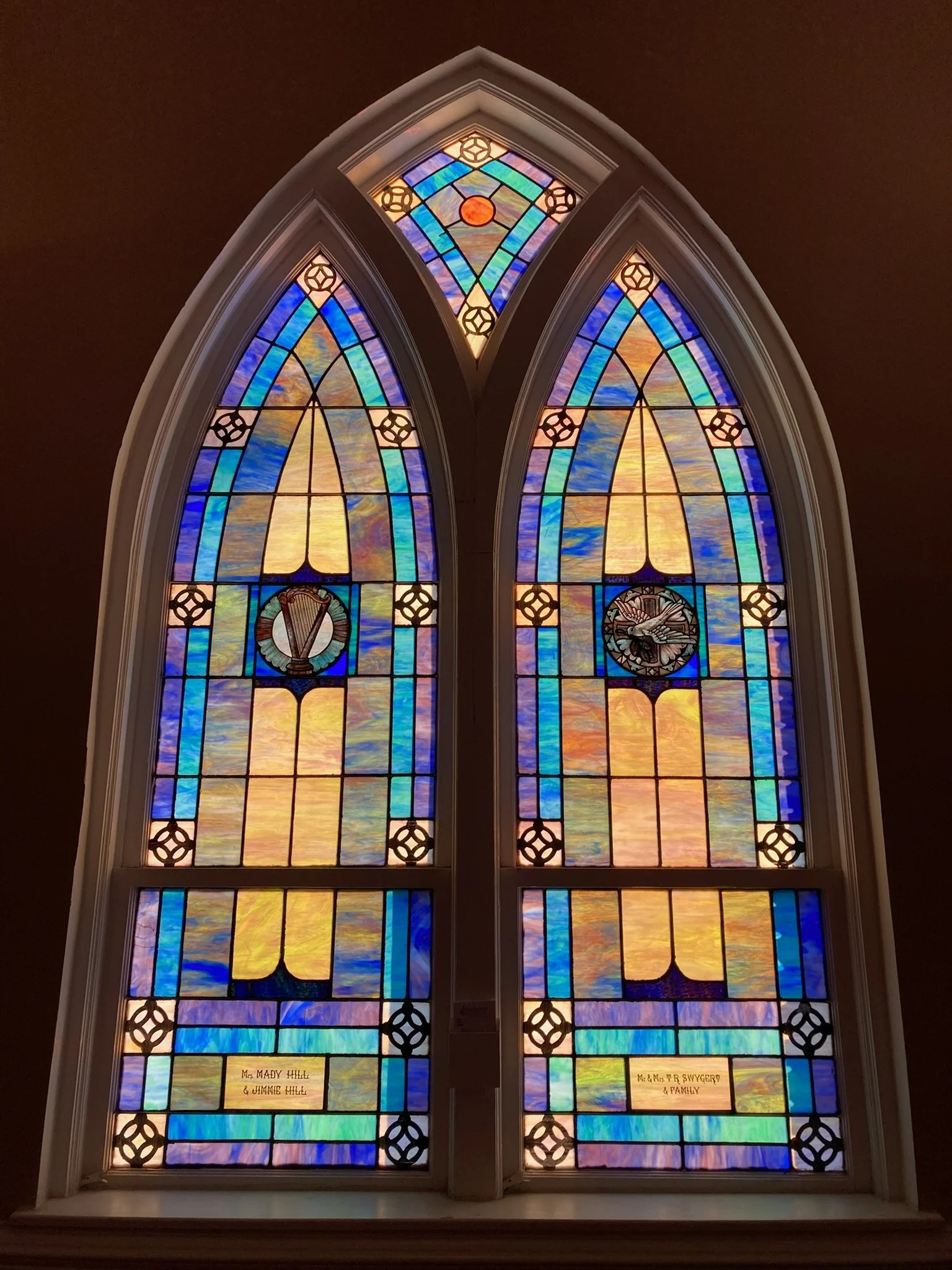 Colorful stained glass window with various designs and text panels at the bottom.