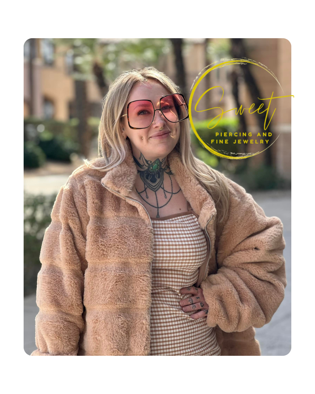 A woman with blonde hair and tattoos, wearing large pink sunglasses and a beige faux fur jacket, standing outdoors in front of buildings and trees, with a logo that says 'Sweet Piercing and Fine Jewelry' in yellow cursive and print.