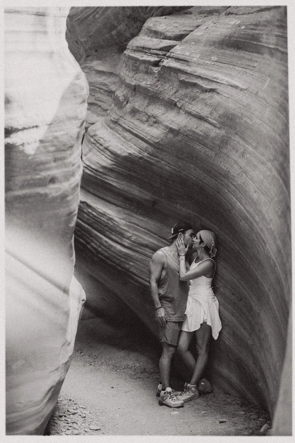 A couple kissing inside a narrow, curved slot canyon with textured rock walls.