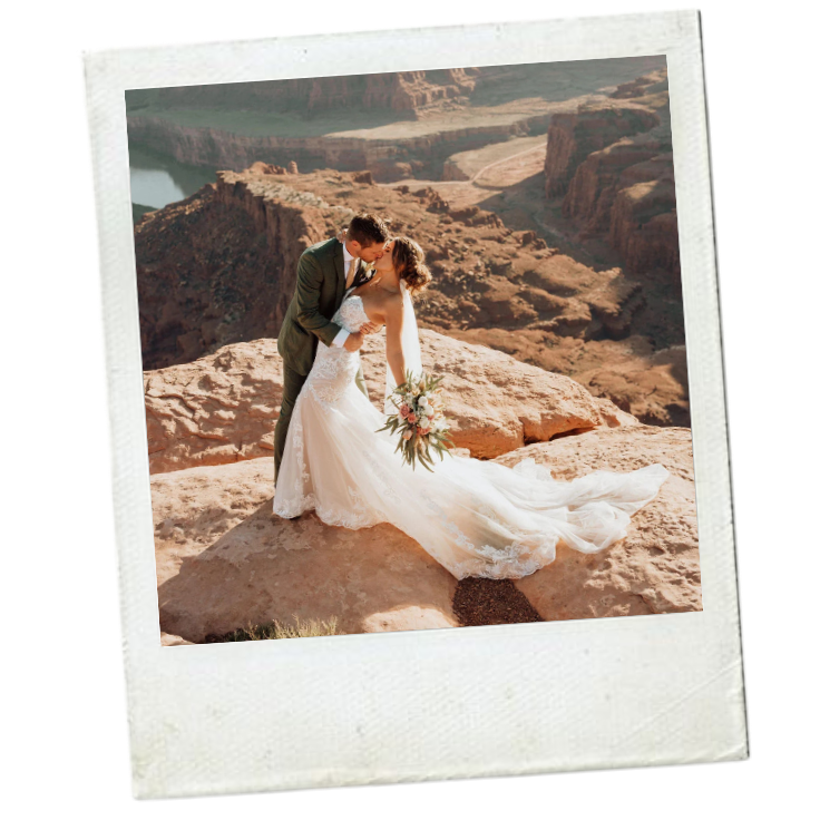 A bride and groom sharing a kiss on a rocky outcrop overlooking a canyon with rugged terrain and a river below, during sunset.