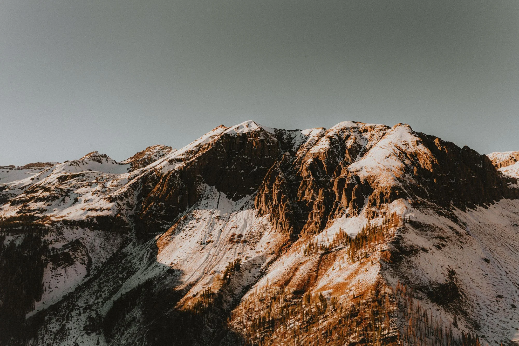 Snow-covered mountain peaks in Colorado under a clear sky during sunset.