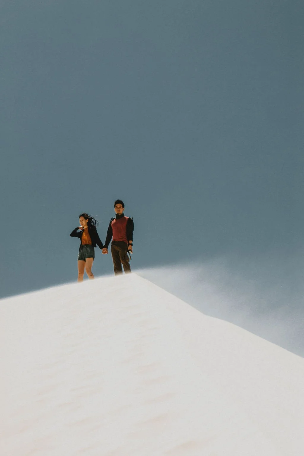 Two people holding hands standing on snowy terrain with clear skies.