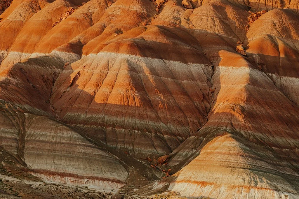 Colorful layered rock formations in a canyon, with shades of orange, red, yellow, and gray.